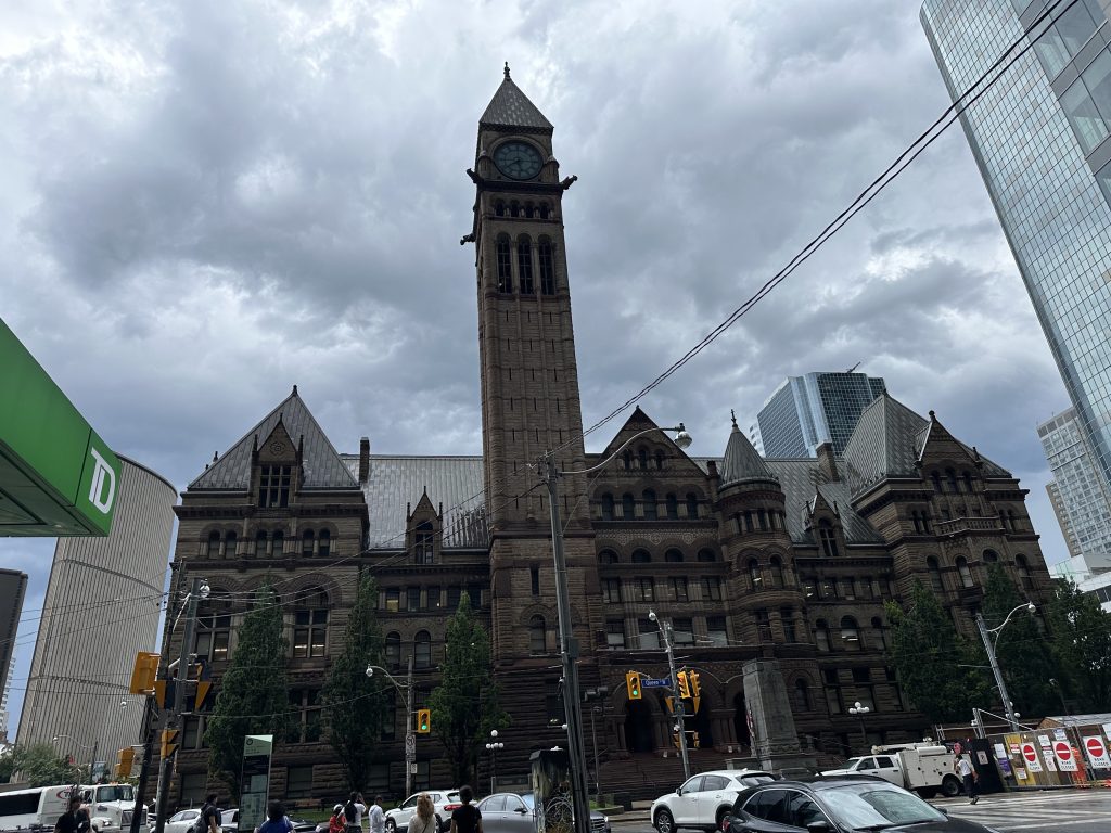 A historic clock-tower building in downtown Toronto under cloudy skies.